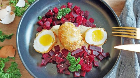 frittierte Eier, zwei Hälften und eins ganz auf auf einem Salatbett mit roter Bete, daneben goldenes Besteck und Eierschalen (Foto: SWR, Jens Alinia )