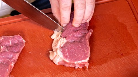 Die zarten Fleischscheiben vom Rind für den Zwiebelrostbraten werden vor dem Braten an der Fettschicht eingeschnitten.