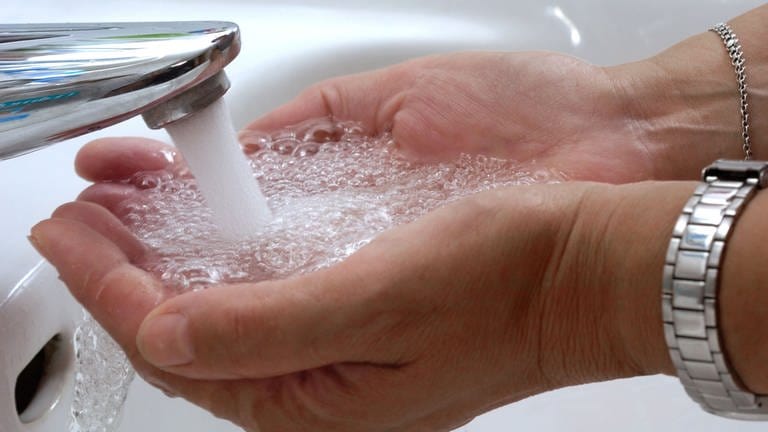 Tipps fürs Wasser sparen im Alltag: Zwei Hände werden in einem Waschbecken unter fließendes Wasser gehalten.