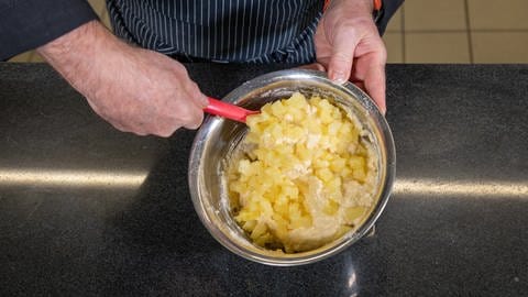 Leckeres Rezept für Ananas-Kokos-Kuchen: Die Ananas wird in kleine Stücke geschnitten und in der silbernen Schüssel unter den Teig gehoben.