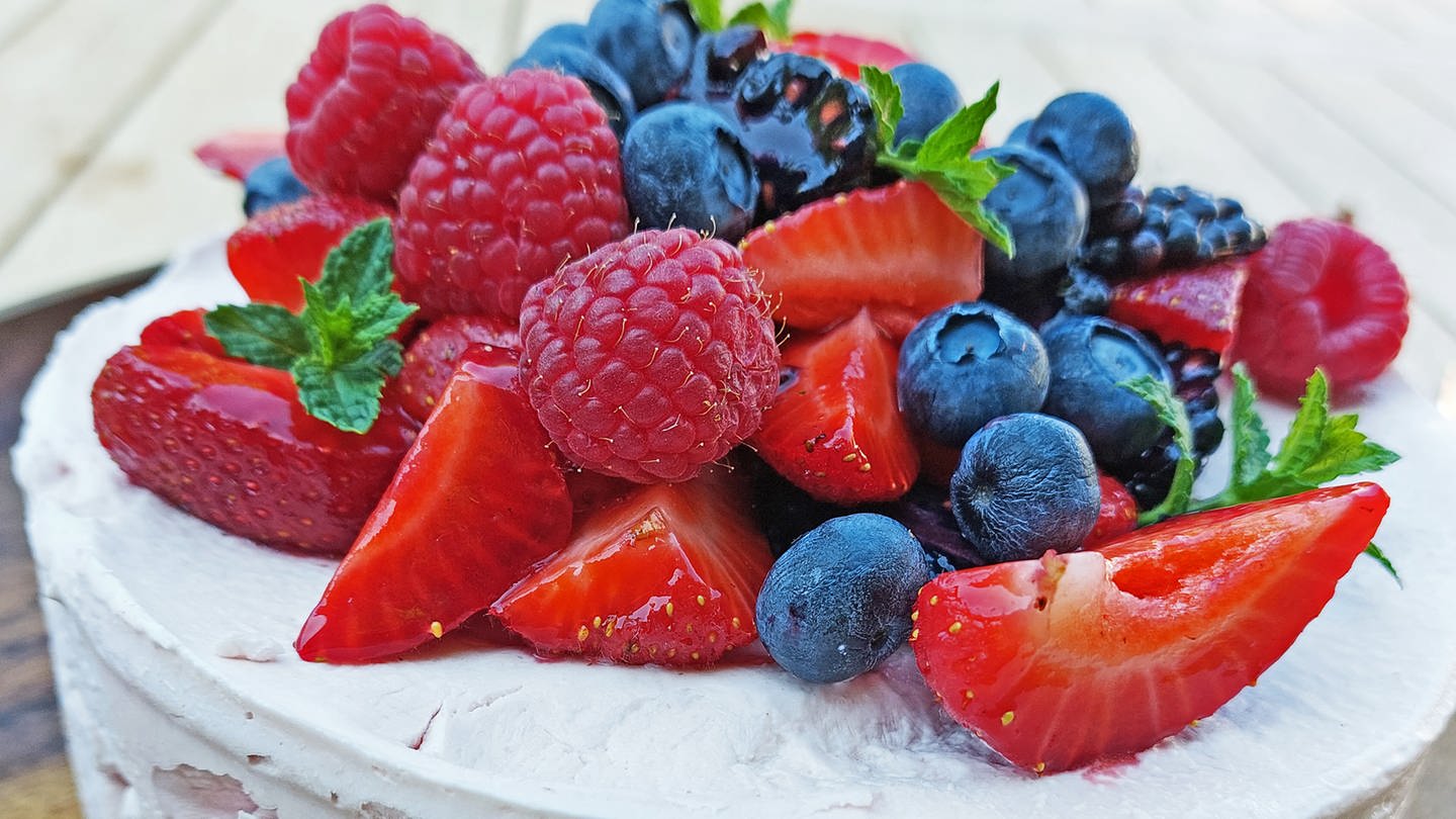 Rezept Eistorte mit Beeren: weiße Torte mit Erdbeeren, Himbeeren, Blaubeeren obenauf, dazu Blätter von Minze als Deko (Foto: SWR, Jens Alinia)