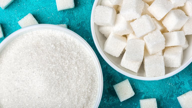 Zucker ist ungesund: Loser Zucker und Zuckerstückchen in Schüsseln aufgehäuft. 