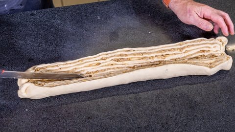 Die mit Marzipan und Walnuss gefüllte Hefeteigrolle wird in der Mitte aufgeschnitten, damit man einen Hefezopf flechten kann. Dieser wird dann zum Hefekranz geformt. (Foto: SWR, Corinna Holzer)