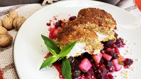 Rezept Hähnchenbrust mit Nusskruste: Stück Hähnchenbrust mit Nusskruste auf rote Bete Salat mit einem Strauß Minze auf einem weißen Teller (Foto: SWR, Märte Burmeister)