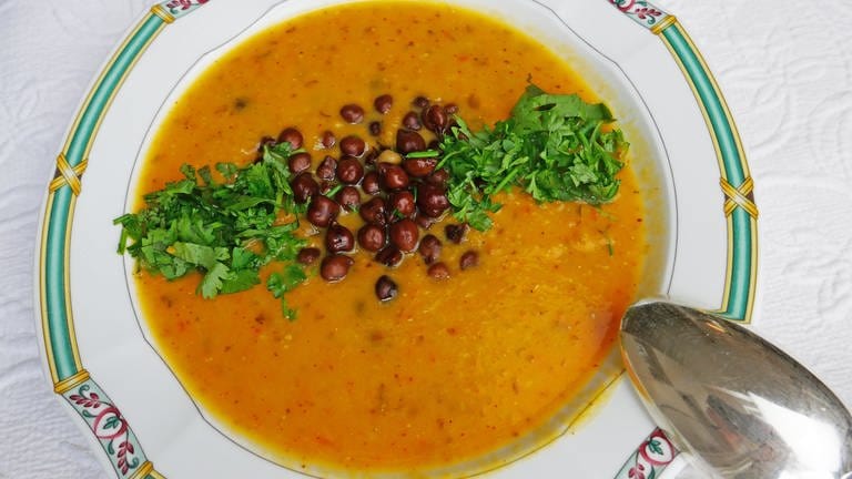Suppenteller mit Musterrand mit braun-oranger Kichererbsensuppe. Als Einlage Kichererbsen und Petersilie