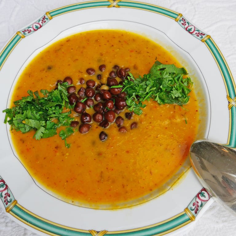 Suppenteller mit Musterrand mit braun-oranger Kichererbsensuppe. Als Einlage Kichererbsen und Petersilie