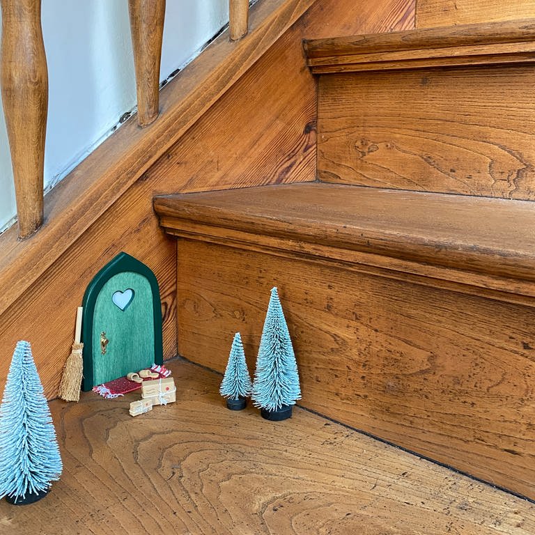 Trend für Weihnachten 2023: Wichteltür auf einer Treppe, kleine Bäume und Geschenke davor