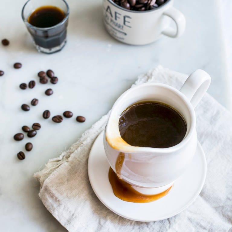 Rezept für Süße Sauce aus Kaffee mit Rum. In einer weißen Karaffe ist dunkle Sauce, daneben liegen Kaffeebohnen.