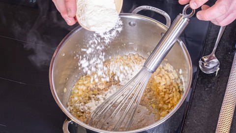 Mehl über Butter und Zwiebel stäuben und eine helle Mehlschwitze erstellen.  