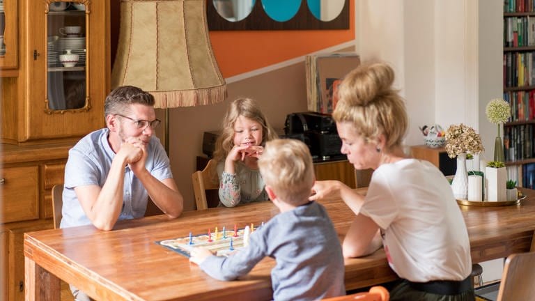 Familie spielt am Tisch gemeinsam ein Brettspiel (Foto: IMAGO, Westend61)