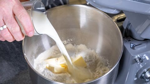 In eine Metallschüssel, in der sich schon Mehl und Butter befinden, wird ein Glas Milch gegossen