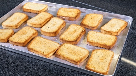 14 goldgelb gebackene Zwiebackscheiben liegen auf einem Metallblech. (Foto: SWR)