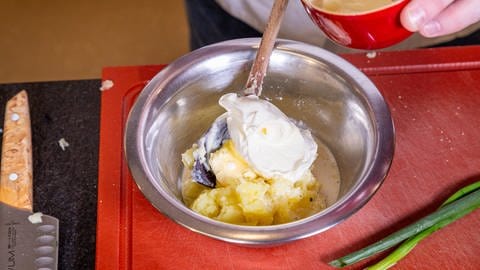Ein großer Klacks weiße Creme liegt auf dem Kartoffelpüree, das sich in einer Metallschale mit Kochlöffel befindet.