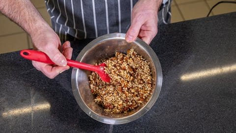In einer Rührschüssel aus Metall sind gehackte Haselnüsse, Mandeln, Zucker und Zimt mit geschmolzener Butter vermischt. (Foto: SWR)