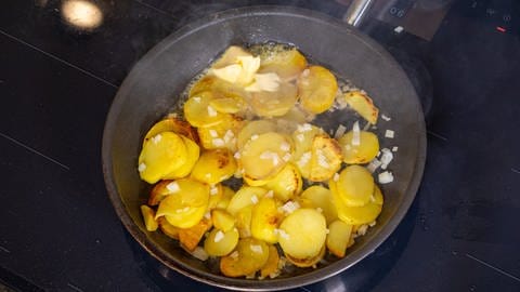 Kartoffelnscheiben braten in einer gusseisernen Pfanne auf dem Herd, kleine Zwiebelwürfel sind untergemischt, die Kartoffeln sind an einigen Stellen schon braun. Lecker in Kombination mit dem Zander. (Foto: SWR)