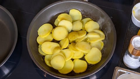 In Scheiben geschnittene Kartoffeln liegen in einer gusseisernen Pfanne, die auf dem Herd steht - die Beilage für den Zander.