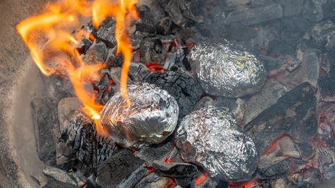 Die Grillkartoffeln liegen in Alufolie verpackt in heißer Grillkohle. Wie im Rezept beschrieben, werden die Kartoffeln dann mit Salsa Sauce serviert.