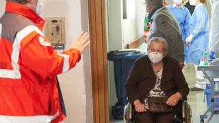 Die 91-jährige Lieselotte Ziegler wird im Altenheim Maria vom Siege im Koblenzer Stadtteil Wallersheim mit ihrem Rollstuhl zur Corona-Impfung gebracht. Die Seniorin ist die erste Rheinland-Pfälzerin, die den Impfstoff erhält. (Foto: dpa Bildfunk, picture alliance/dpa/dpa Pool | Thomas Frey)