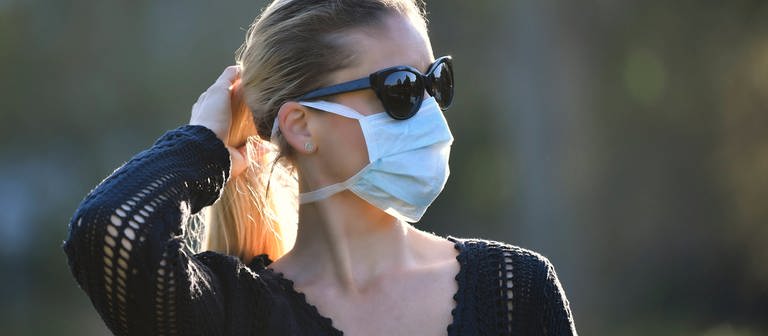 Eine Frau mit Mundschutzmaske traut sich langsam in Corona-Krise Zeiten wieder nach draußen. (Foto: IMAGO, Michael Weber)