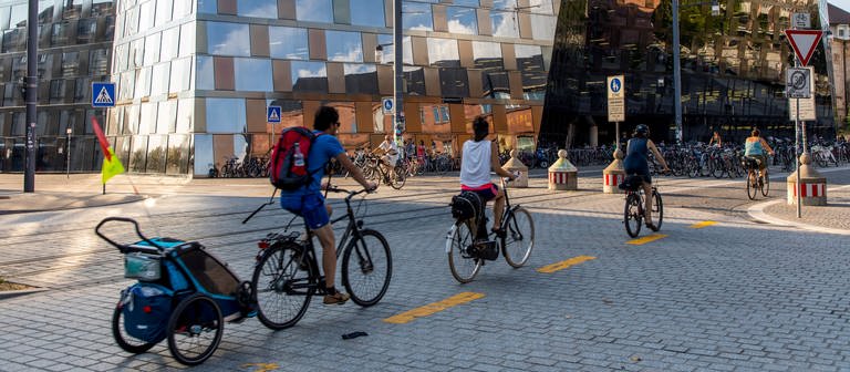 Vor der Universitätsbibliothel in Freiburg fahren mehrere Fahrradfahrer mit sommerlicher Kleidung vorbei (Foto: dpa Bildfunk, Picture Alliance)