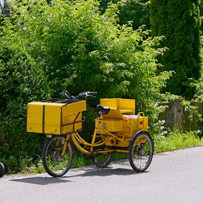 Ein Briefträger der Deutschen Post hat sein Transportrad vor einem Haus abgestellt um die Post an die Haustüre zu bringen. (Foto: IMAGO, MiS)