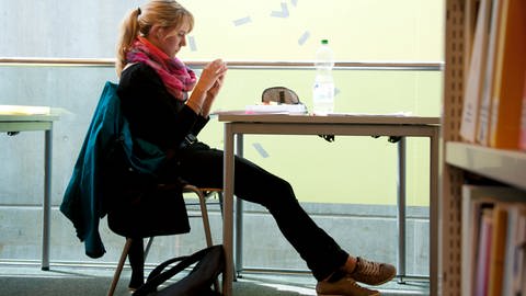 Eine Studentin schaut am 30.06.2014 in Tübingen (Baden-Württemberg) in der Uni-Bibliothek auf ihr Mobiltelefon. Langes Aufschieben von unliebsamen Aufgaben kann für Studenten zum Stress führen. (Foto: picture-alliance / Reportdienste, dpa Bildfunk, Lena Klimkeit)