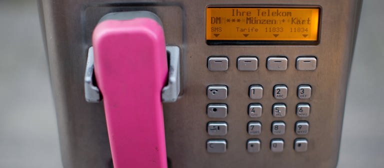Ein Hörer in der Farbe Magenta hängt an einem öffentlichen Telekom-Münztelefon.  (Foto: picture-alliance / Reportdienste, dpa Bildfunk, Martin Gerten)