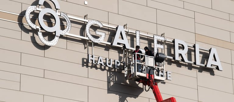 Arbeiter montieren ein "Galeria"-Logo - bald könnte es wieder abgenommen werden. (Foto: dpa Bildfunk, picture alliance/dpa | Boris Roessler)