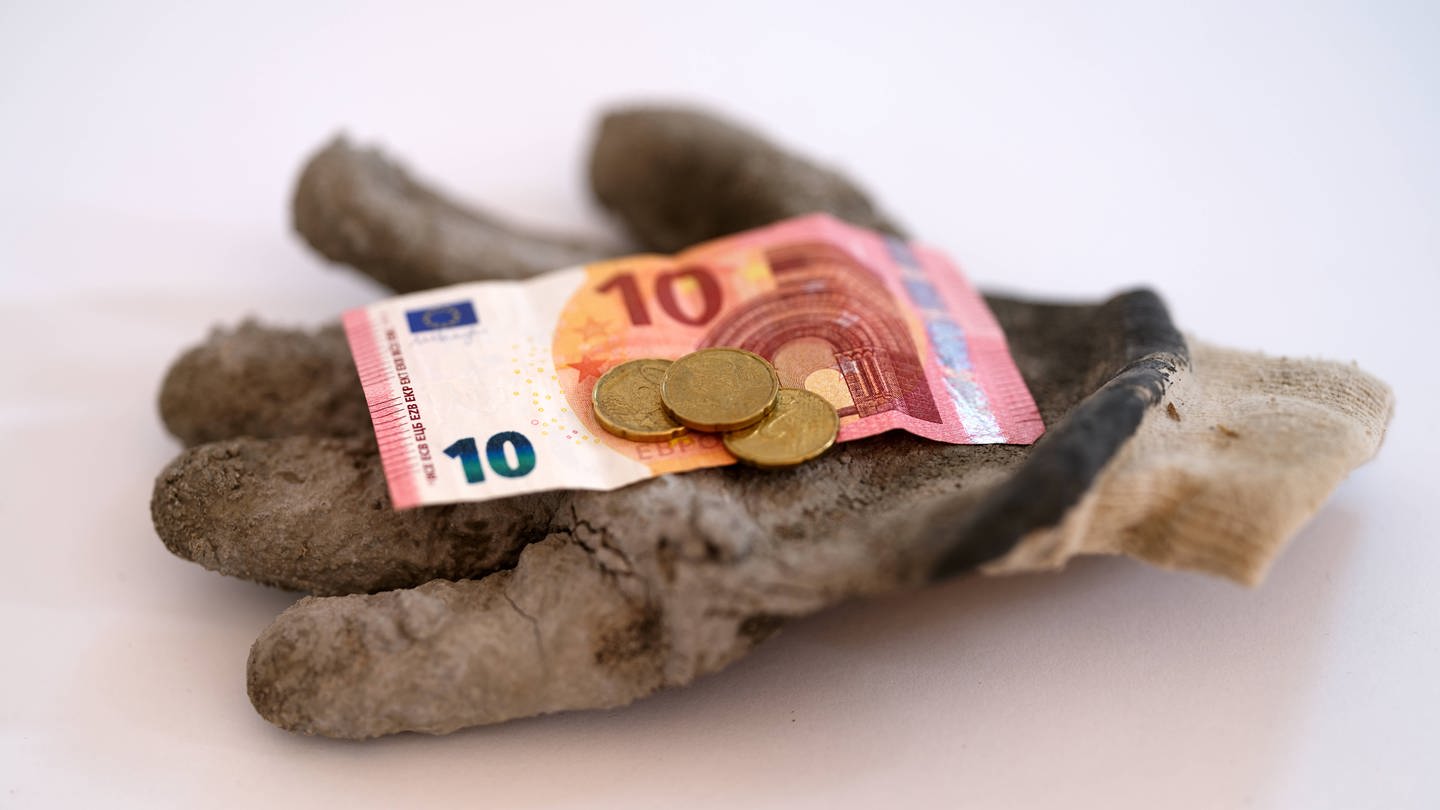 Bargeld liegt auf einen Arbeitshandschuh (Foto: IMAGO, IMAGO / serienlicht)