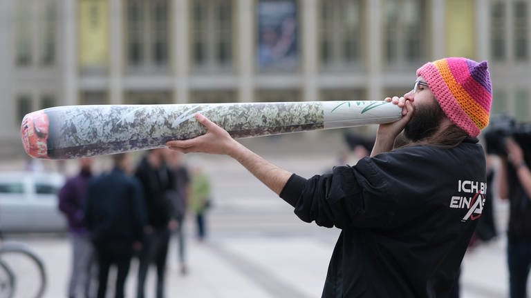 Ein Teilnehmer einer Kundgebung hält einen überdimensionierten Joint in den Händen. Ab dem 1. April 2024 ist Erwachsenen ab 18 Jahren der Besitz von 25 Gramm im öffentlichen Raum erlaubt. (Foto: dpa Bildfunk, Picture Alliance)
