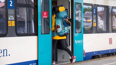 Eine Frau mit Rucksack steigt am Morgen am Bahnhof in eine Regionalbahn.
