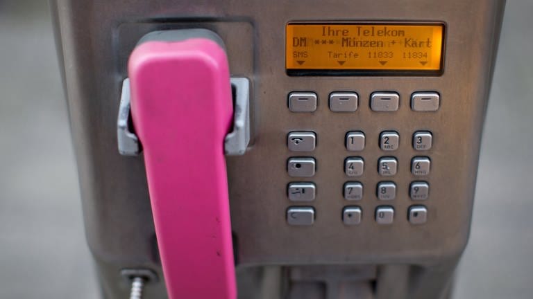 Ein Hörer in der Farbe Magenta hängt an einem öffentlichen Telekom-Münztelefon.  (Foto: picture-alliance / Reportdienste, dpa Bildfunk, Martin Gerten)