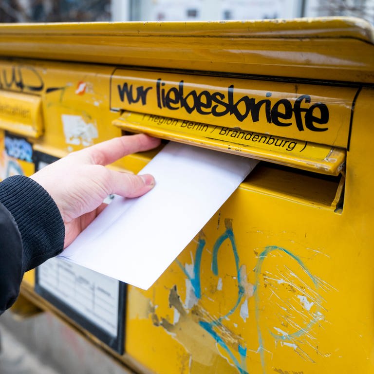 Ein Mann wirft einen Brief in einen Briefkasten. 