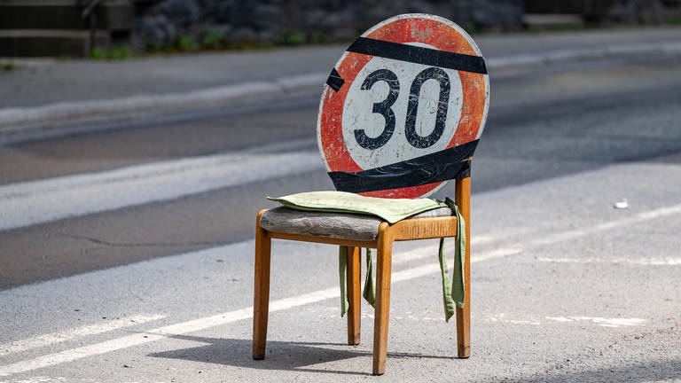 Ein Verkehrsschild das auf eine Tempo-30-Zone hinweist, wurde an einem Stuhl befestigt, der auf der Straße steht.