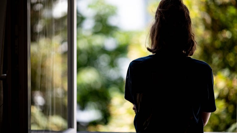 Eine Frau steht in ihrer Wohnung an einem Fenster. (Foto: picture-alliance / Reportdienste, dpa Bildfunk, Fabian Sommer)