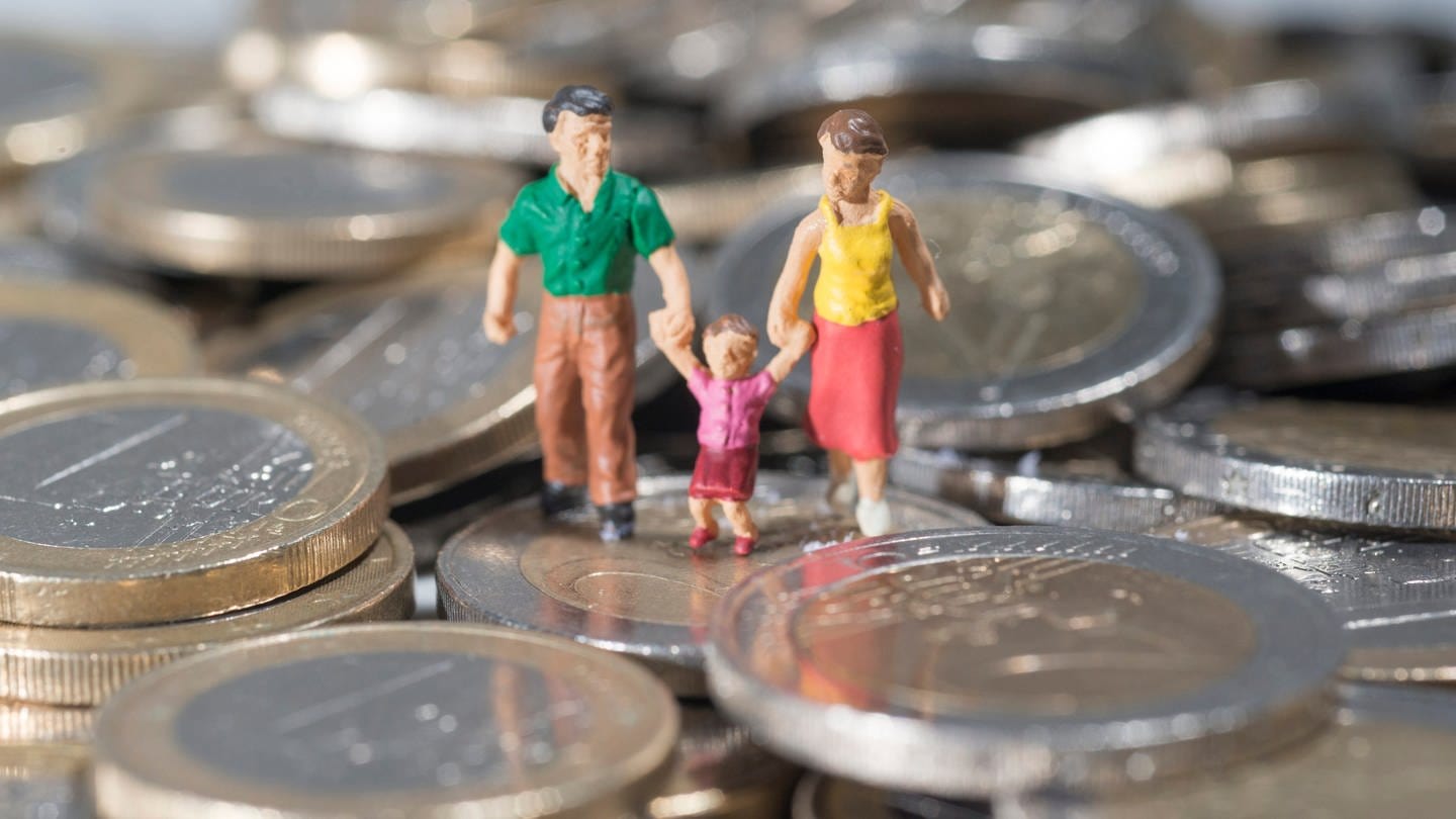 Eine Familie aus Spielfiguren ist auf einem Haufen Euromünzen zu sehen. (Foto: picture-alliance / Reportdienste, dpa Bildfunk, Marc Müller)