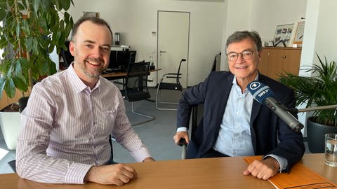 Korrespondent Oliver Neuroth und Ralph Tiesler sitzen beim Interview in Bonn in einem Büro an einem Tisch vor einem SWR Mikrofon nebeneinander und schauen in die Kamera (Foto: SWR, Foto: Marianne Suntrup, Bundesamt für Bevölkerungsschutz und Katastrophenhilfe)