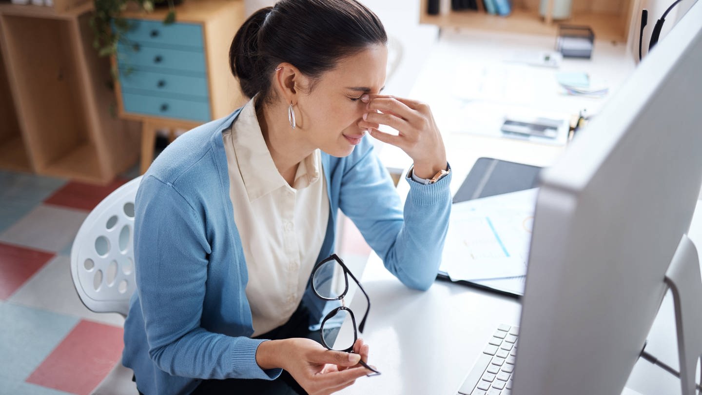 Eine junge Frau sieht gestresst aus, während sie an einem Laptop an ihrem Schreibtisch arbeitet (Foto: IMAGO, Zoonar II)