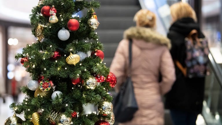 Kunden gehen in einem Einkaufszentrum an einem geschmückten Weihnachtsbaum vorbei