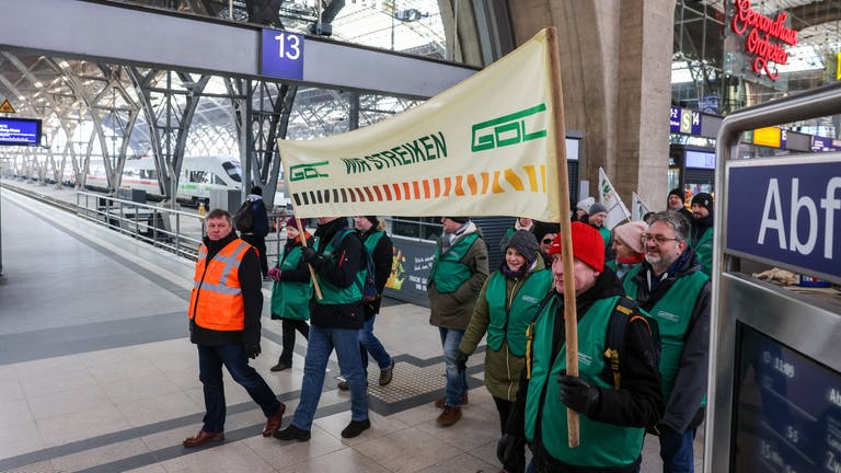 Mitglieder der Lokführergewerkschaft GDL gehen mit einem Banner mit der Aufschrift "Wir streiken" durch ein Bahnhofsgebäude.
