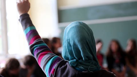 Ein Mädchen mit einem Kopftuch ist von hinten in einem Klassenzimmer zu sehen