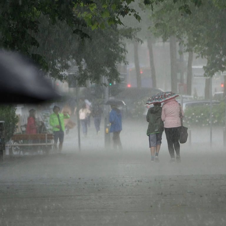 Menschen laugen unter Regenschirmen bei Starkregen