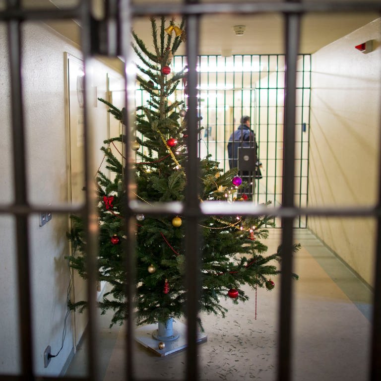Auf einem mit einem Weihnachtsbaum geschmückten Gefängnisflur schließt ein Justizvollzugsbeamter eine Zellentür ab. Rechtzeitig zu Weihnachten zeigt sich die Justiz in vielen Bundesländern gnädig und entlässt Hunderte Häftlinge vorzeitig aus dem Gefängnis. (Foto: dpa Bildfunk, picture alliance | Frank Rumpenhorst)