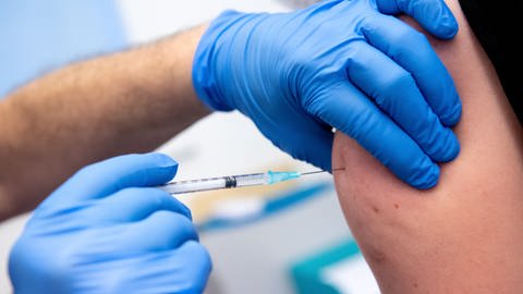 Ein Mitarbeiter in einer Klinik wird von einem Kollegen mit dem Corona-Impfstoff von BioNTechPfizer geimpft.  (Foto: dpa Bildfunk, picture alliance/dpa | Sven Hoppe)