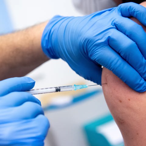Ein Mitarbeiter in einer Klinik wird von einem Kollegen mit dem Corona-Impfstoff von BioNTechPfizer geimpft.  (Foto: dpa Bildfunk, picture alliance/dpa | Sven Hoppe)
