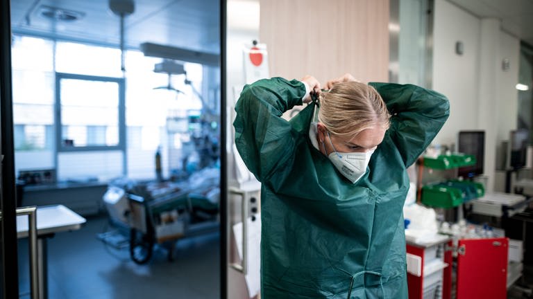 Eine Gesundheits- und Krankenpflegerin steht auf dem Gang einer Corona-Intensivstation eines Klinikums und zieht sich Schutzkleidung an.  (Foto: dpa Bildfunk, picture alliance/dpa | Fabian Strauch)