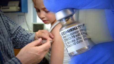 Fotomontage: Ein Kind wird geimpft. Im Vordergrund ist ein Fläschchen mit einem Covid-19-Impfstoff zu sehen.  (Foto: IMAGO, IMAGO / Sven Simon (Fotomontage) )
