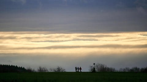 Spaziergänger sind vor einem wolkenverhangenen Himmel zu sehen. Der Deutsche Wetterdienst erwartet für Baden-Württemberg Dauerregen und Sturmböen.  (Foto: dpa Bildfunk, picture alliance/dpa | Thomas Warnack)