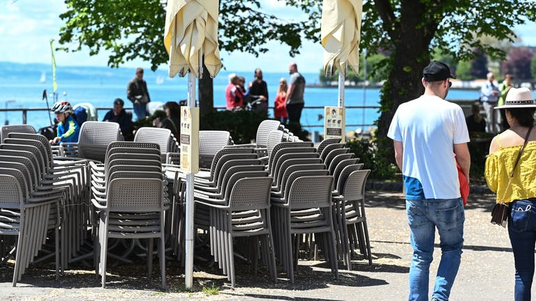 Stühle und Tische stehen aufgereiht an der Uferpromenade, während im Hintergrund Passanten laufen. (Foto: dpa Bildfunk, picture alliance/dpa | Felix Kästle)