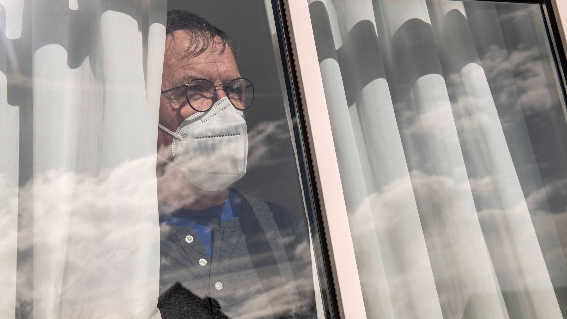 Mann steht an einem Fenster, weil er sich nach einem positivem Corona-Test zu Hause isolieren muss. (Foto: IMAGO, IMAGO / Wolfgang Maria Weber)
